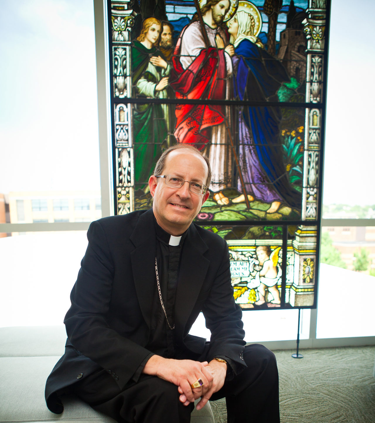 Bishop Walkowiak sits in front of stained glass window on fourth floor of Cathedral Square Center