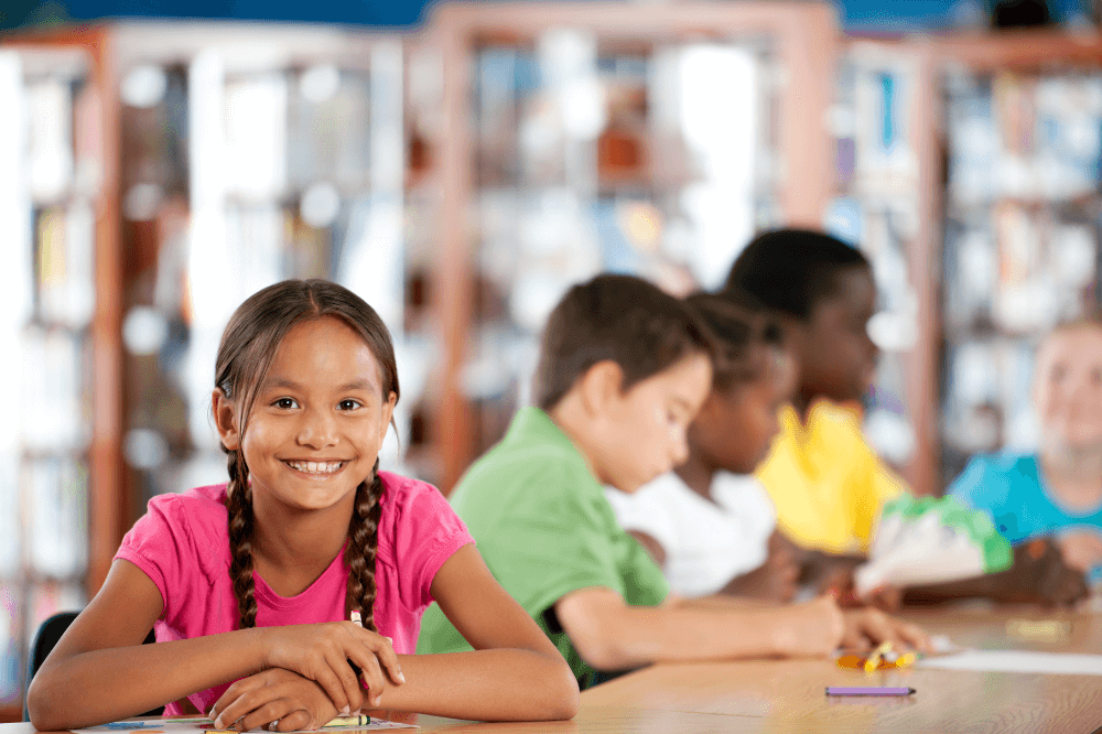 Elementary student smiles as peers study in the background in school library