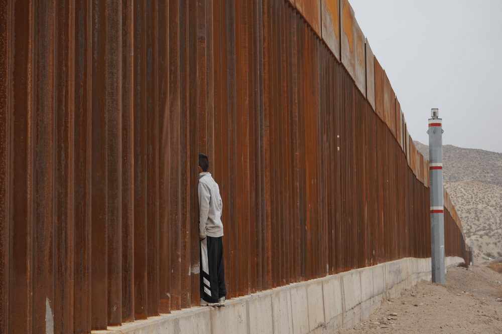 Boy looks through fence at border